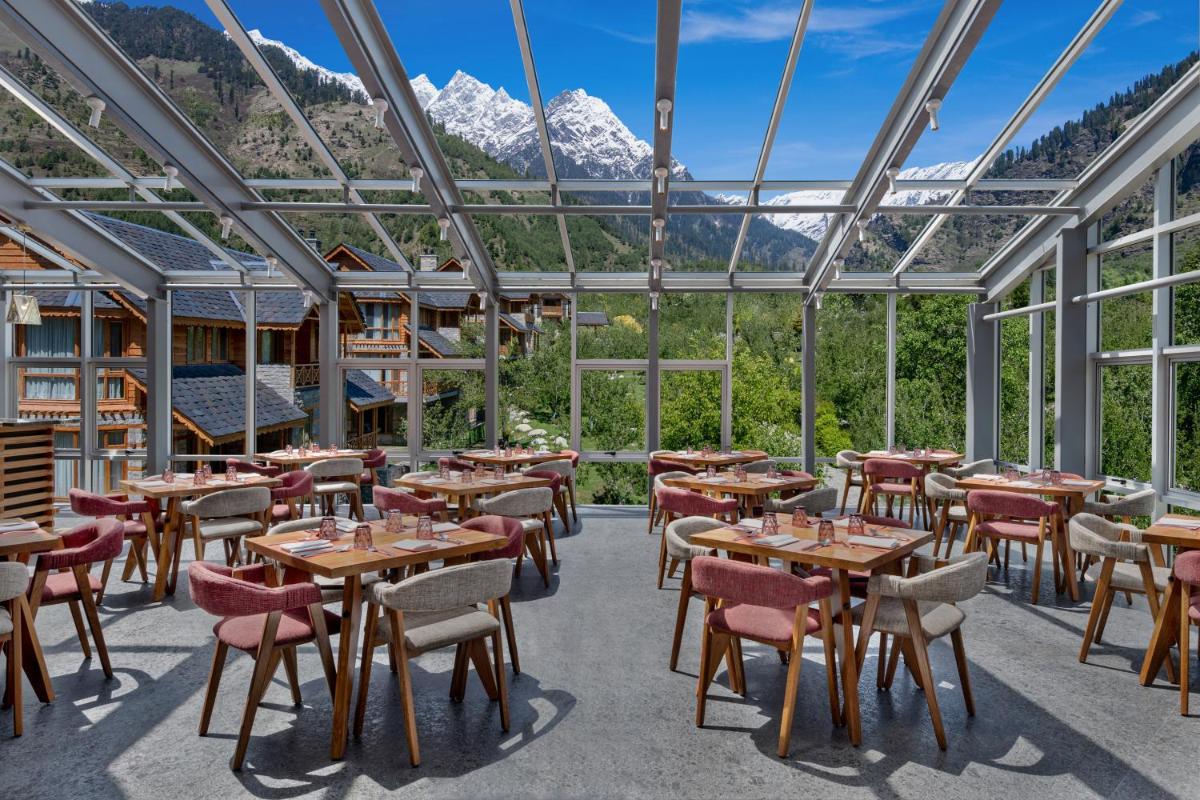 a restaurant with tables and chairs and mountains in the background at Welcomhotel By ITC Hotels, Hamsa Manali in Manāli a restaurant with tables and chairs and mountains in the background at Welcomhotel By ITC Hotels, Hamsa Manali in Manāli