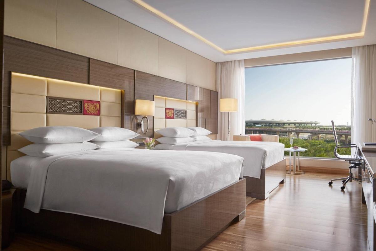 a hotel room with three beds and a large window at JW Marriott Mumbai Sahar Airport in Mumbai a hotel room with three beds and a large window at JW Marriott Mumbai Sahar Airport in Mumbai