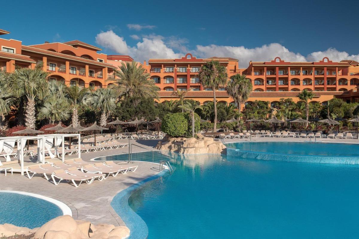 Un complejo con piscina y sillas y un edificio. en Sheraton Fuerteventura Golf & Spa Resort, en Caleta de Fuste