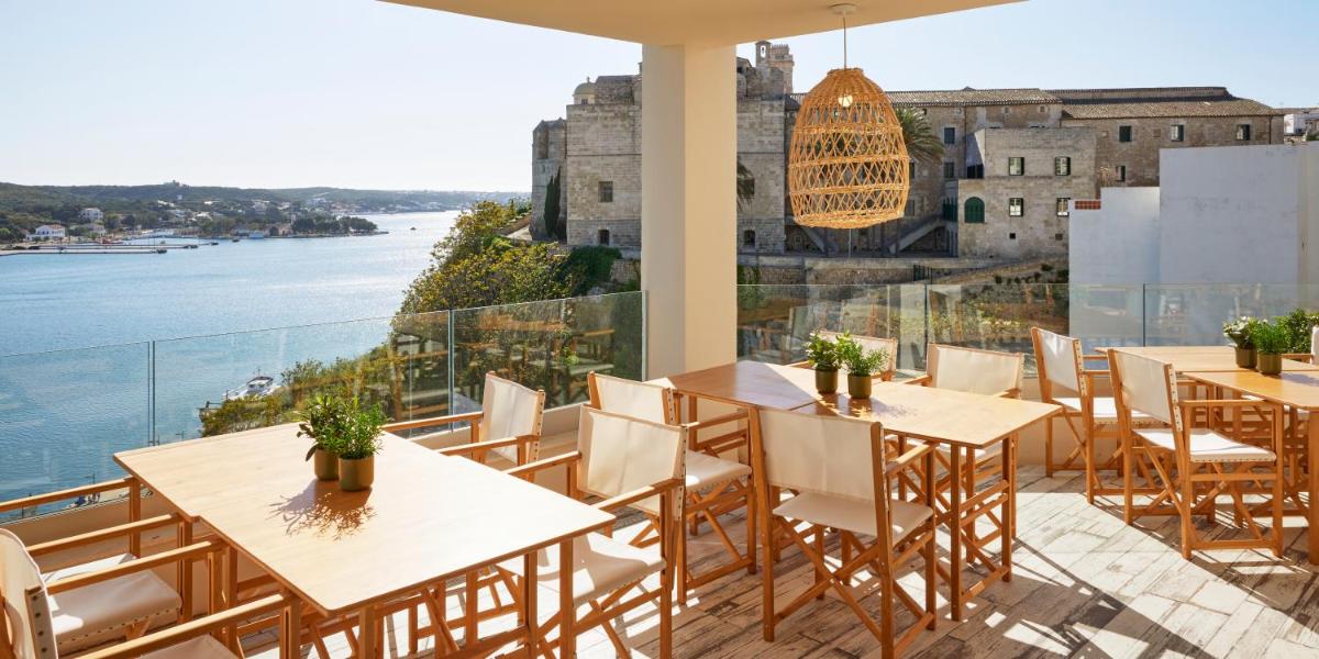 Un restaurante con mesas y sillas y vista al agua. en Catalonia Mirador des Port, en Mahón