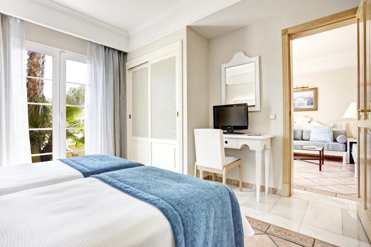 Un dormitorio con una cama, un escritorio y un televisor. en Grupotel Playa Club, en Son Xoriguer
