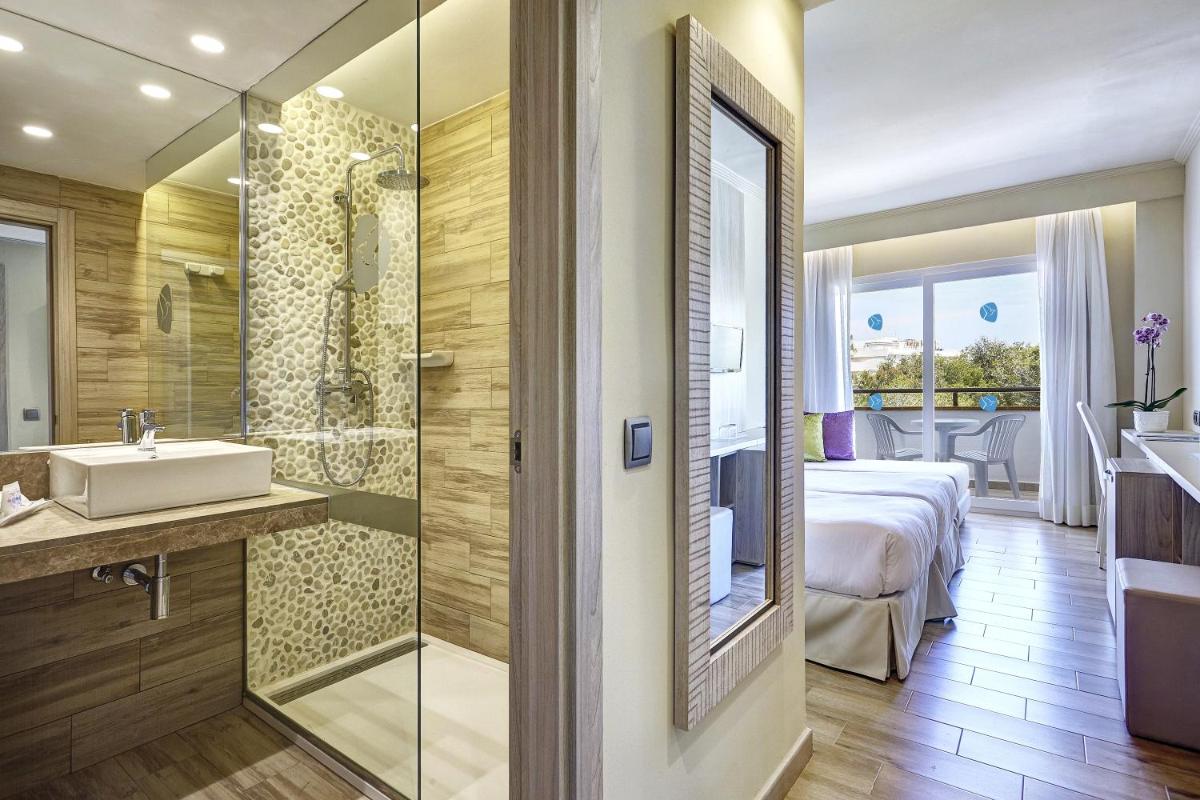 Un baño con lavabo y ducha y una cama. en Grupotel Maritimo, en Puerto de Alcudia