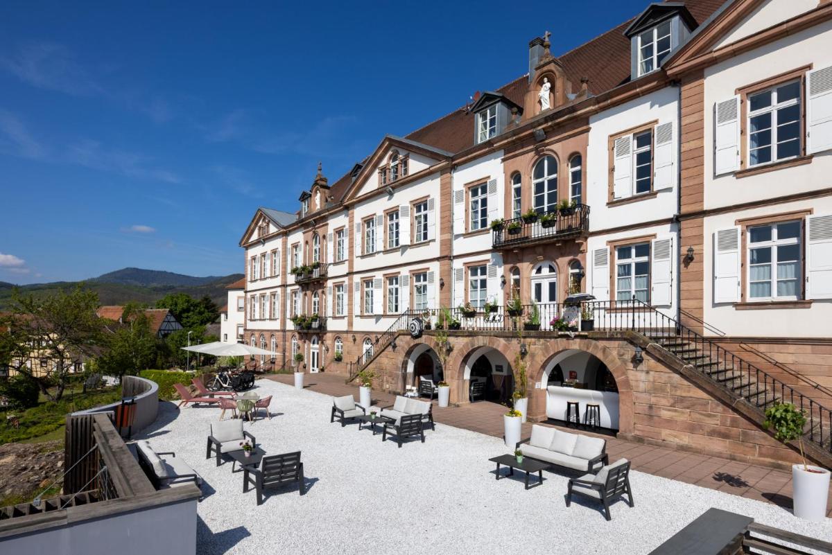 un grand bâtiment avec des chaises et des tables dans une cour dans l'établissement Hôtel Val-Vignes Colmar Haut-Koenigsbourg, The Originals Relais, à Saint-Hippolyte
