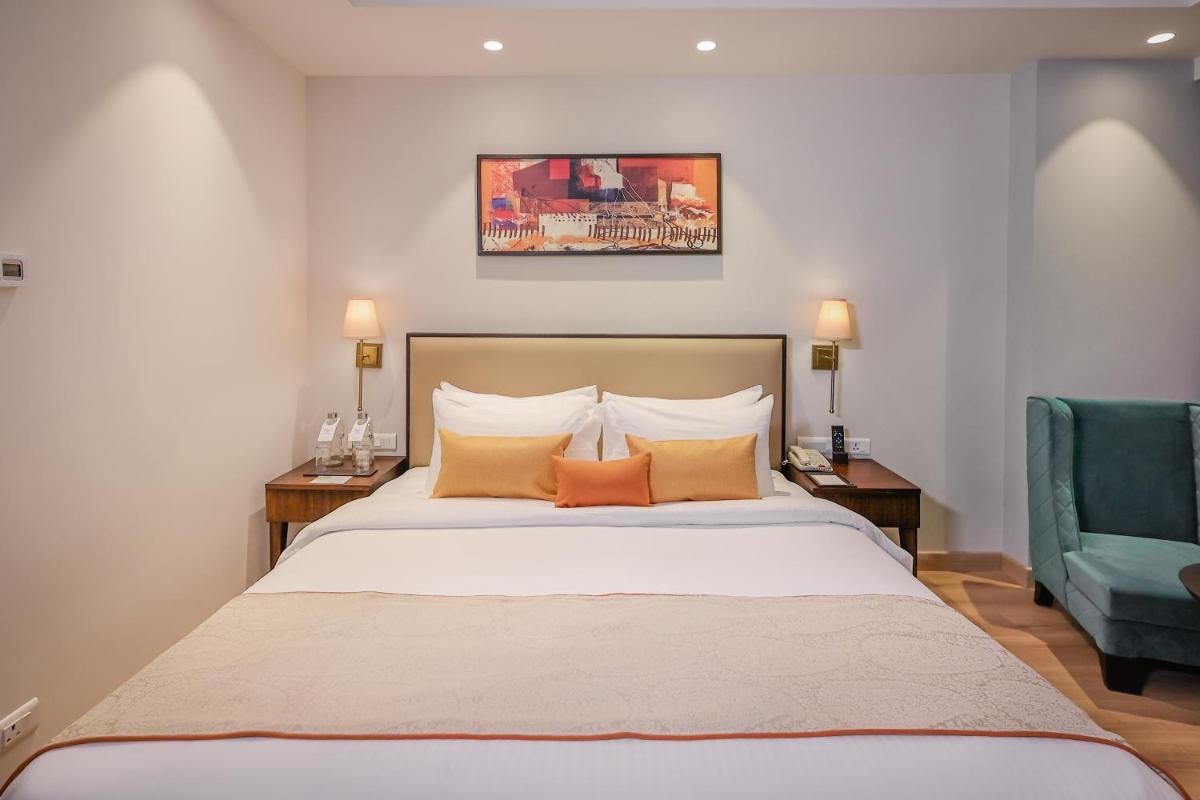 a bedroom with a large bed with two tables and a green chair at Regenta Dehradun by Royal Orchid Hotels Limited in Dehradun
