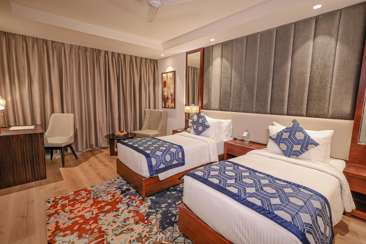 a hotel room with two beds and a desk at Regenta Dehradun by Royal Orchid Hotels Limited in Dehradun