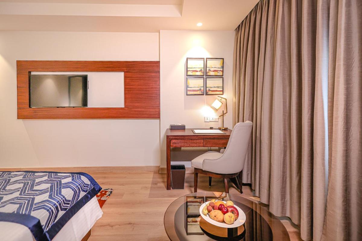 a hotel room with a bed and a desk with a bowl of fruit at Regenta Dehradun by Royal Orchid Hotels Limited in Dehradun
