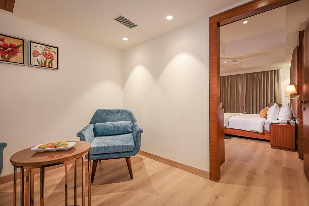 a room with a chair and a table and a bed at Regenta Dehradun by Royal Orchid Hotels Limited in Dehradun