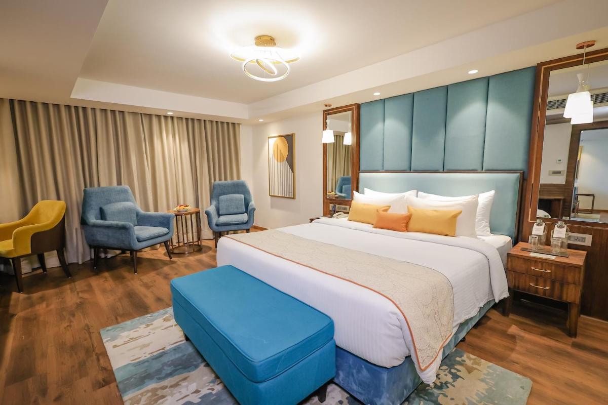 a hotel room with a large bed and blue chairs at Regenta Dehradun by Royal Orchid Hotels Limited in Dehradun