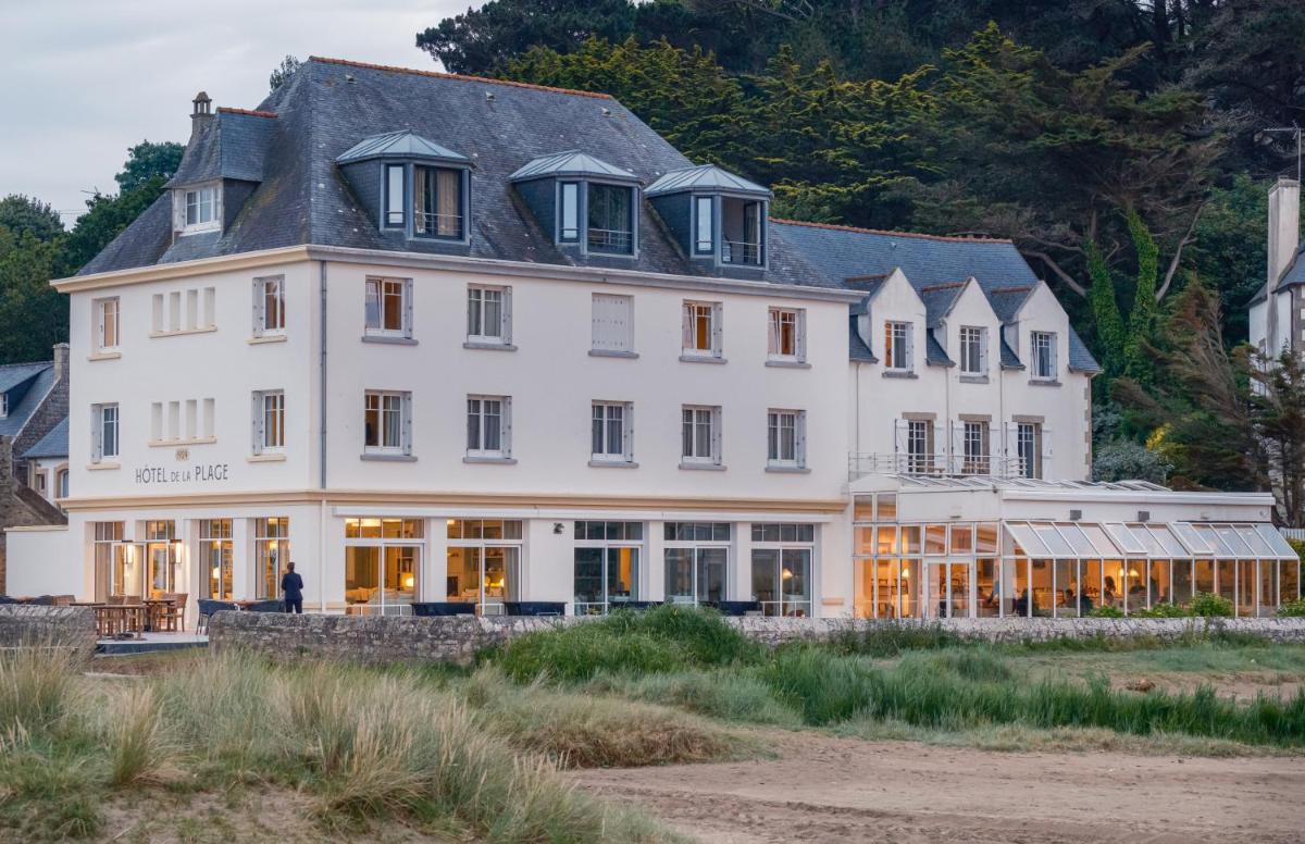 un grand bâtiment blanc avec un homme debout devant lui dans l'établissement Hôtel de la Plage, à Plonévez-Porzay