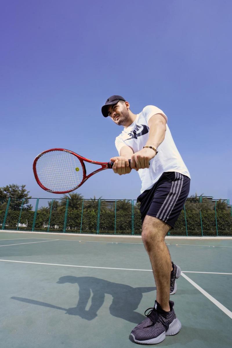 a man holding a tennis racket on a tennis court at BLVD Club - Near BENGALURU AIRPORT in Bengaluru