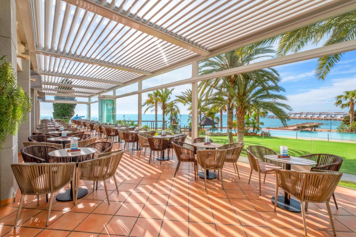 Un patio con mesas y sillas y el mar. en Gran Hotel Las Fuentes, en Alcossebre