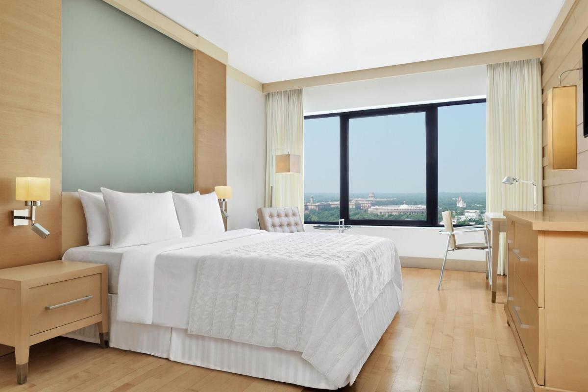 a bedroom with a white bed and a large window at Le Meridien New Delhi in New Delhi a bedroom with a white bed and a large window at Le Meridien New Delhi in New Delhi