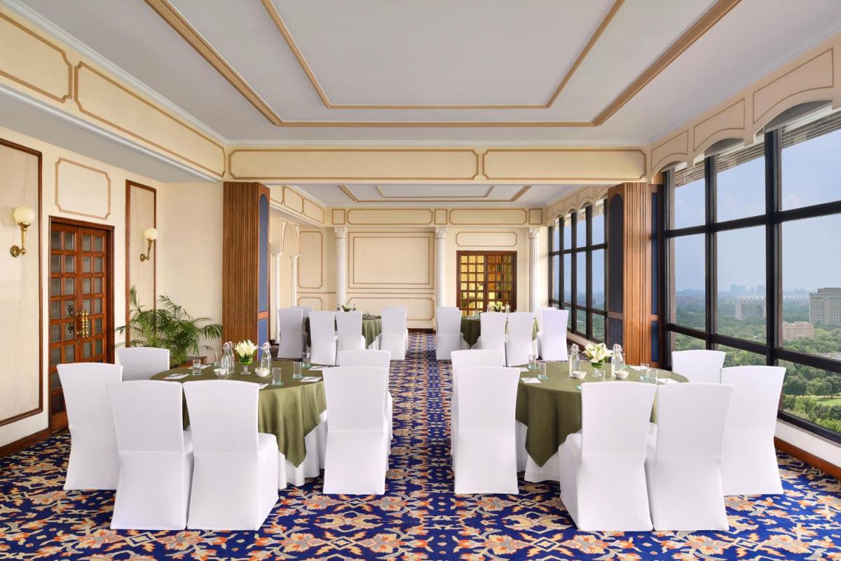 a room with tables and white chairs and windows at Le Meridien New Delhi in New Delhi a room with tables and white chairs and windows at Le Meridien New Delhi in New Delhi
