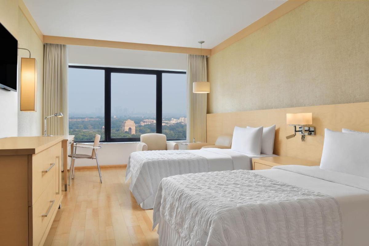 a hotel room with two beds and a large window at Le Meridien New Delhi in New Delhi a hotel room with two beds and a large window at Le Meridien New Delhi in New Delhi