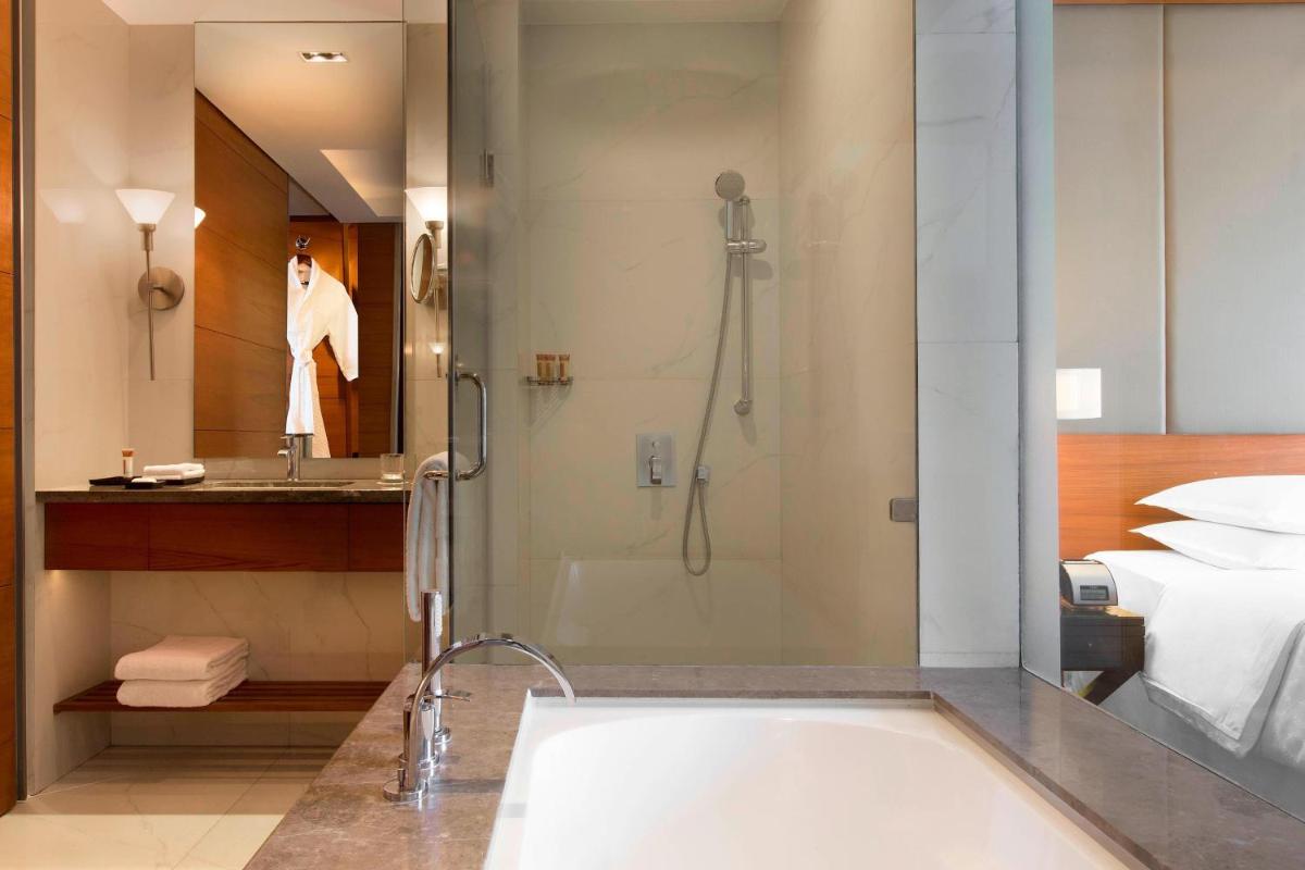 a bathroom with a tub and a shower and a bed at Sheraton Hyderabad Hotel in Hyderabad