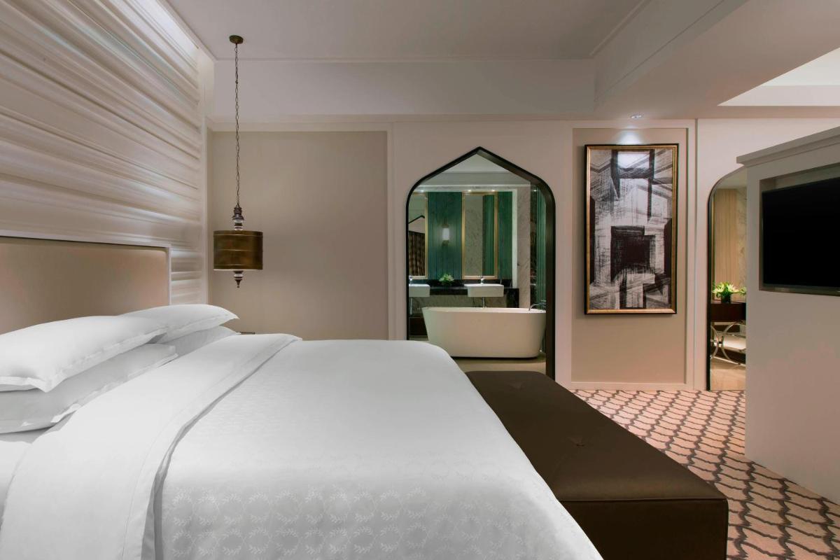 a bedroom with a large white bed and a bathroom at Sheraton Hyderabad Hotel in Hyderabad