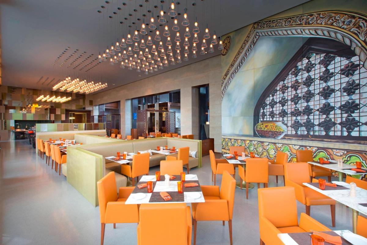 a dining room with orange chairs and tables at Sheraton Hyderabad Hotel in Hyderabad