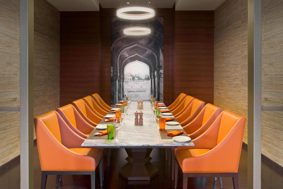 a long dining room with orange chairs and a long table at Sheraton Hyderabad Hotel in Hyderabad