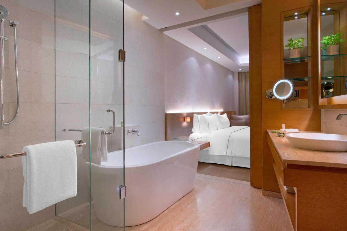 a bathroom with a bath tub and a bedroom at The Westin Mumbai Garden City in Mumbai