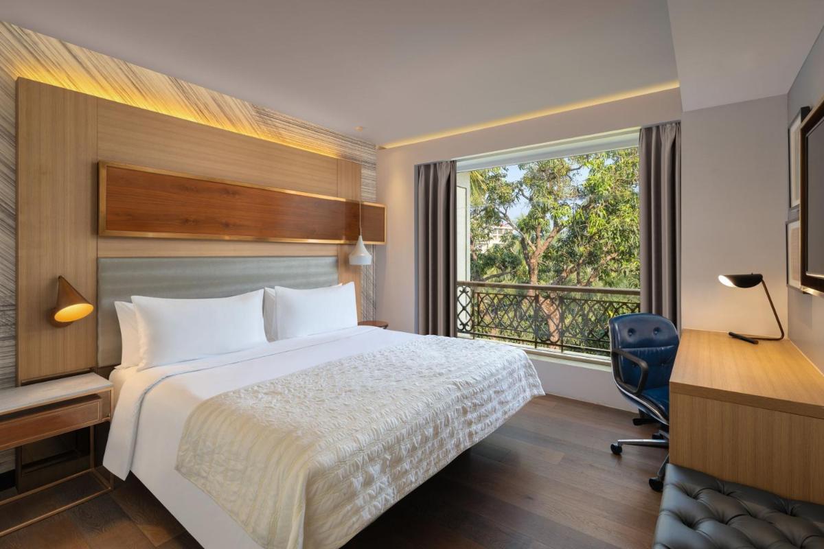 a hotel room with a bed and a desk and a window at Le Meridien Goa, Calangute in Calangute a hotel room with a bed and a desk and a window at Le Meridien Goa, Calangute in Calangute