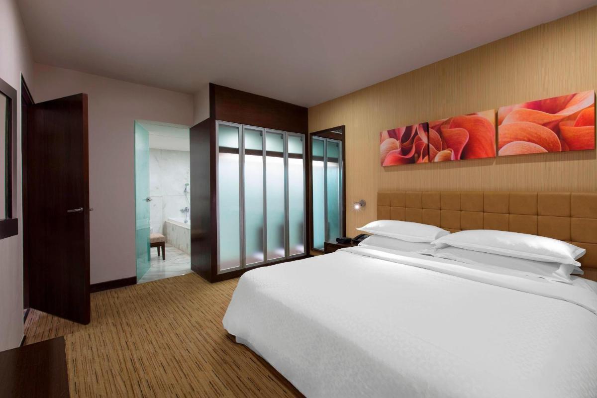 a bedroom with a large white bed and a bathroom at Four Points by Sheraton Hotel and Serviced Apartments Pune in Pune