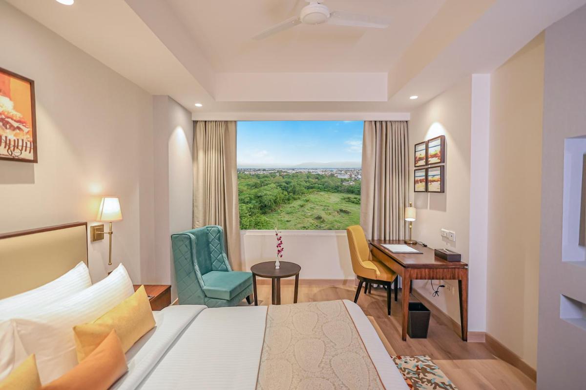 a hotel room with a bed and a desk and a window at Regenta Dehradun by Royal Orchid Hotels Limited in Dehradun