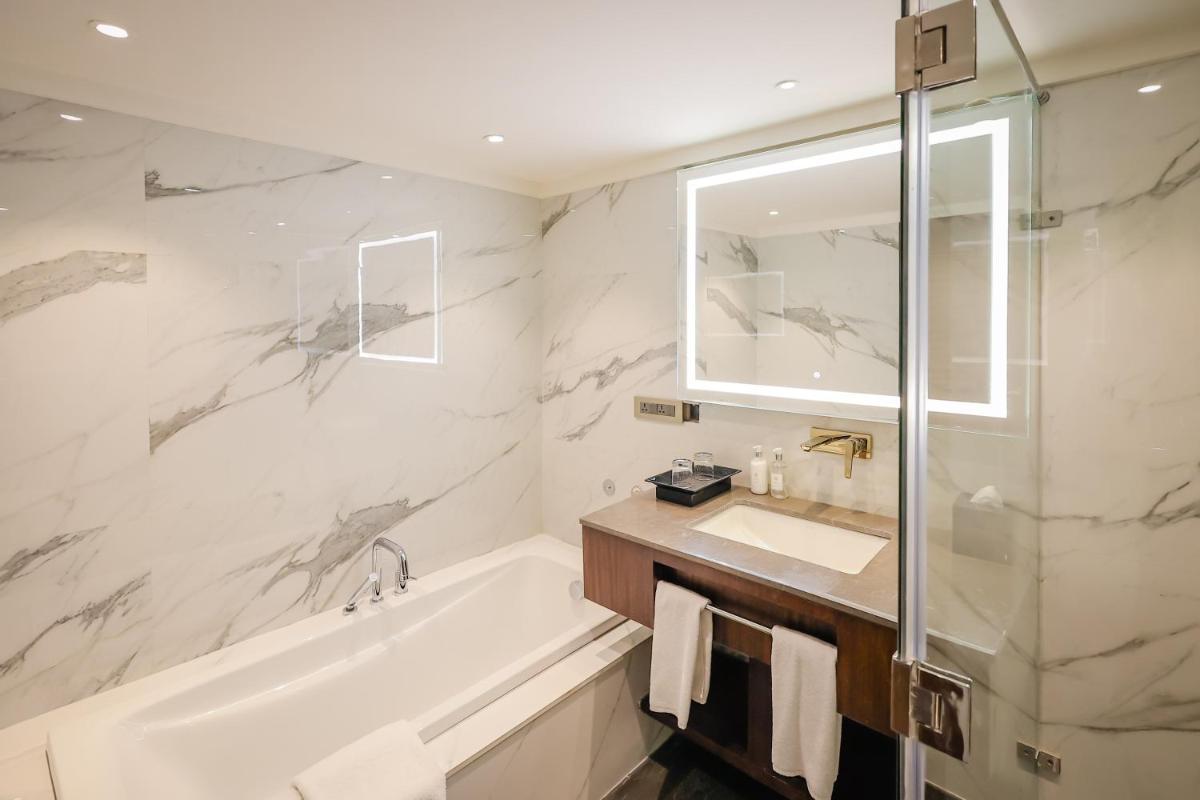 a bathroom with a tub and a sink and a mirror at Regenta Dehradun by Royal Orchid Hotels Limited in Dehradun