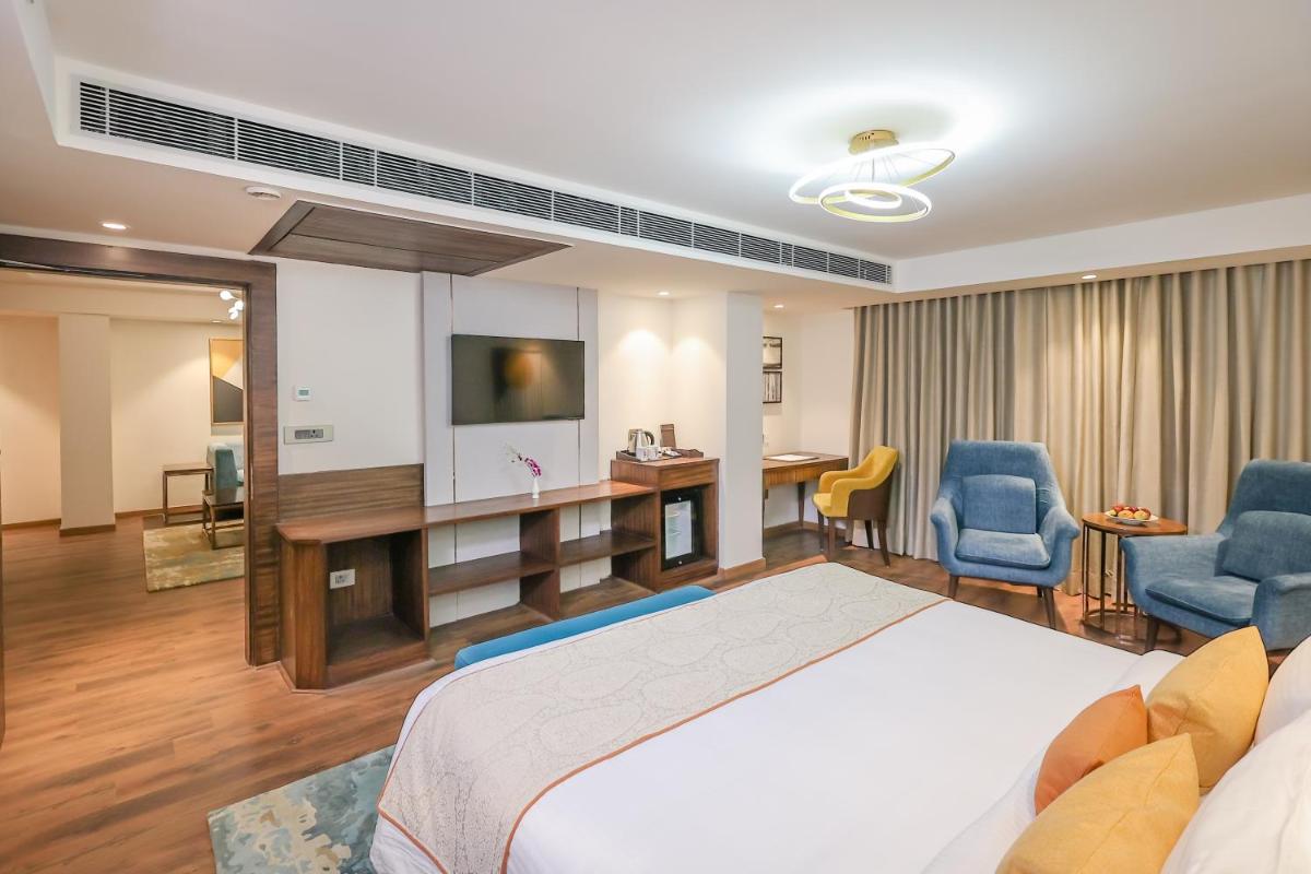 a hotel room with a bed and a tv and chairs at Regenta Dehradun by Royal Orchid Hotels Limited in Dehradun