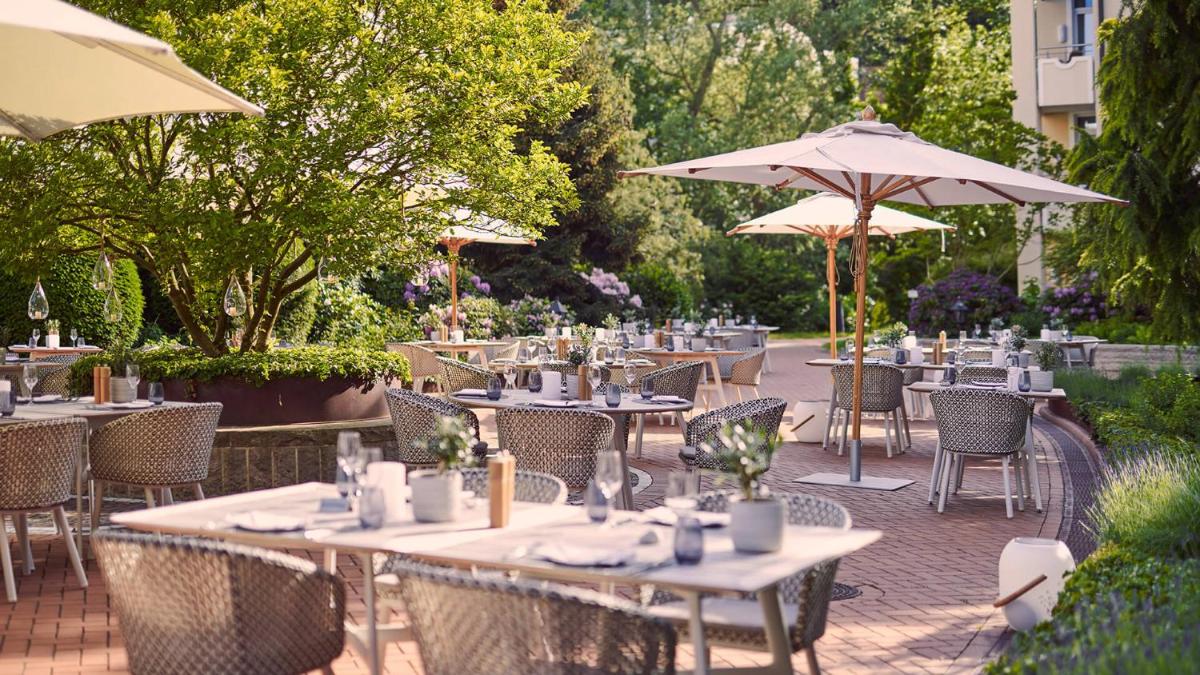 eine Außenterrasse mit Tischen, Stühlen und Sonnenschirmen in der Unterkunft VILA VITA Rosenpark in Marburg an der Lahn eine Außenterrasse mit Tischen, Stühlen und Sonnenschirmen in der Unterkunft VILA VITA Rosenpark in Marburg an der Lahn