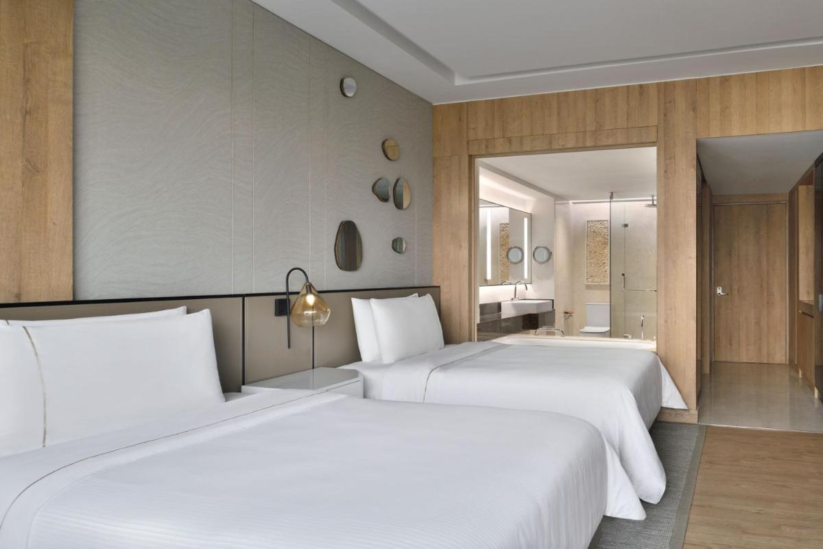 two beds in a hotel room with white sheets at The Westin Mumbai Powai Lake in Mumbai