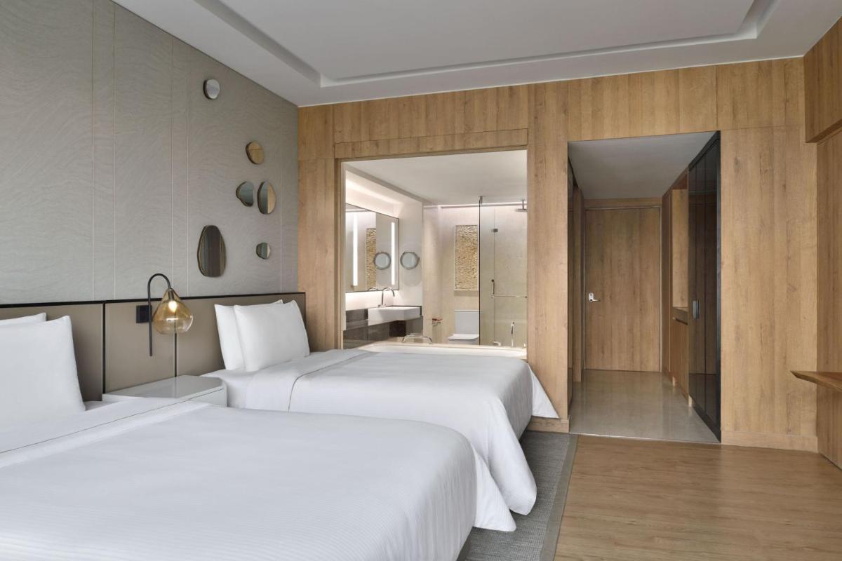 a bedroom with two beds and a bathroom with a mirror at The Westin Mumbai Powai Lake in Mumbai