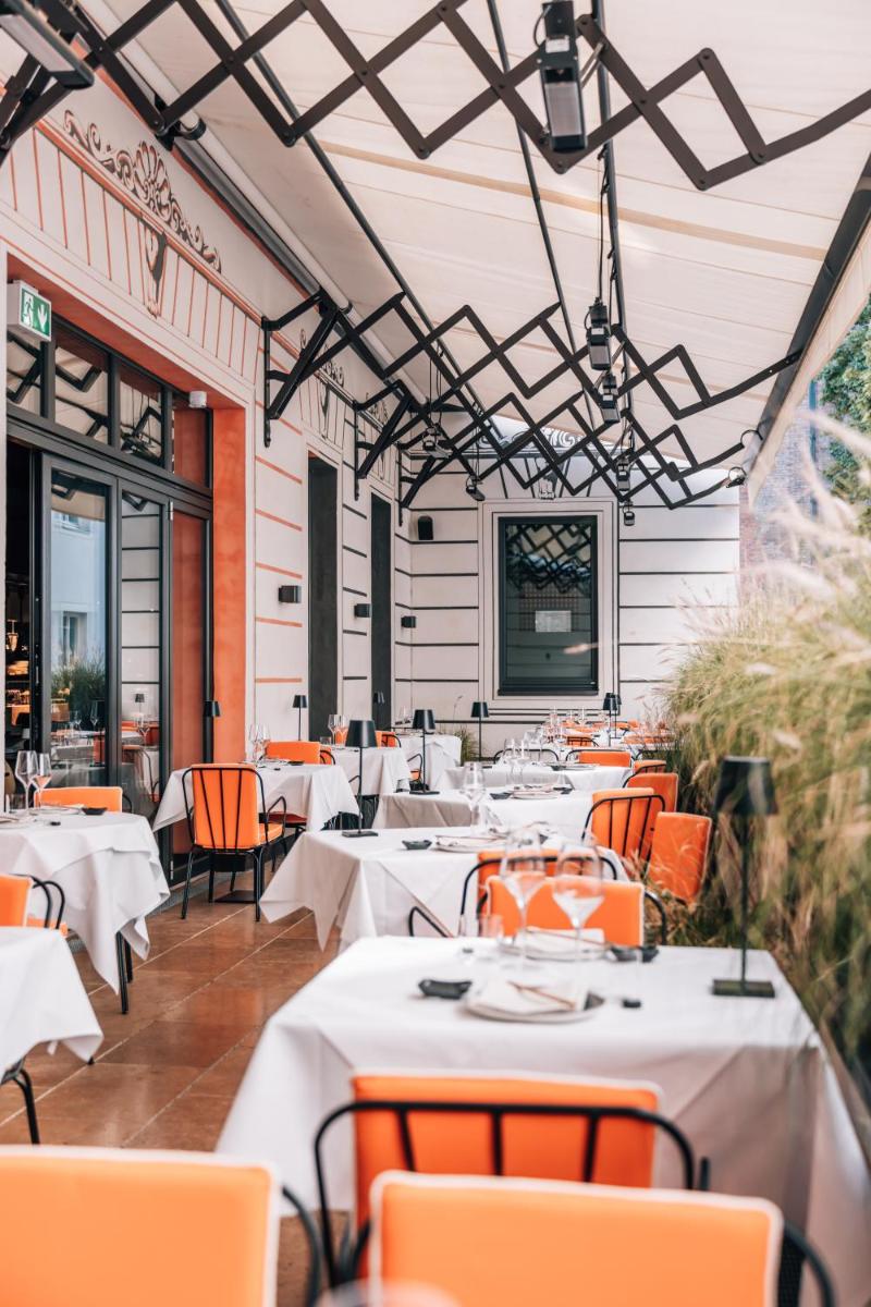 ein Restaurant mit weißen Tischen und orangefarbenen Stühlen in der Unterkunft DO & CO Hotel München in München ein Restaurant mit weißen Tischen und orangefarbenen Stühlen in der Unterkunft DO & CO Hotel München in München