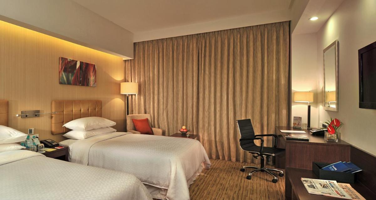 a hotel room with two beds and a desk at Four Points by Sheraton Hotel and Serviced Apartments Pune in Pune