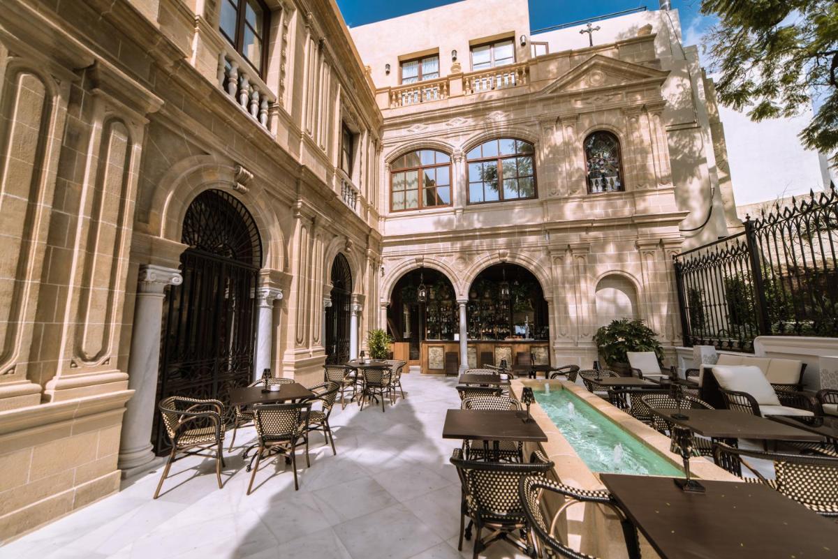 Un patio con mesas y sillas y un edificio. en Hotel Casa Palacio María Luisa, en Jerez de la Frontera