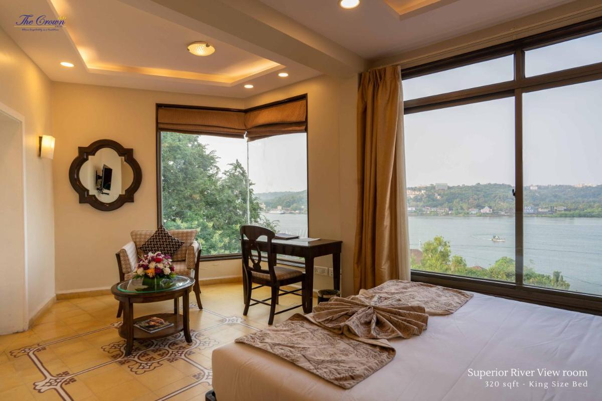 a bedroom with two beds and a desk and a large window at The Crown Goa in Panaji