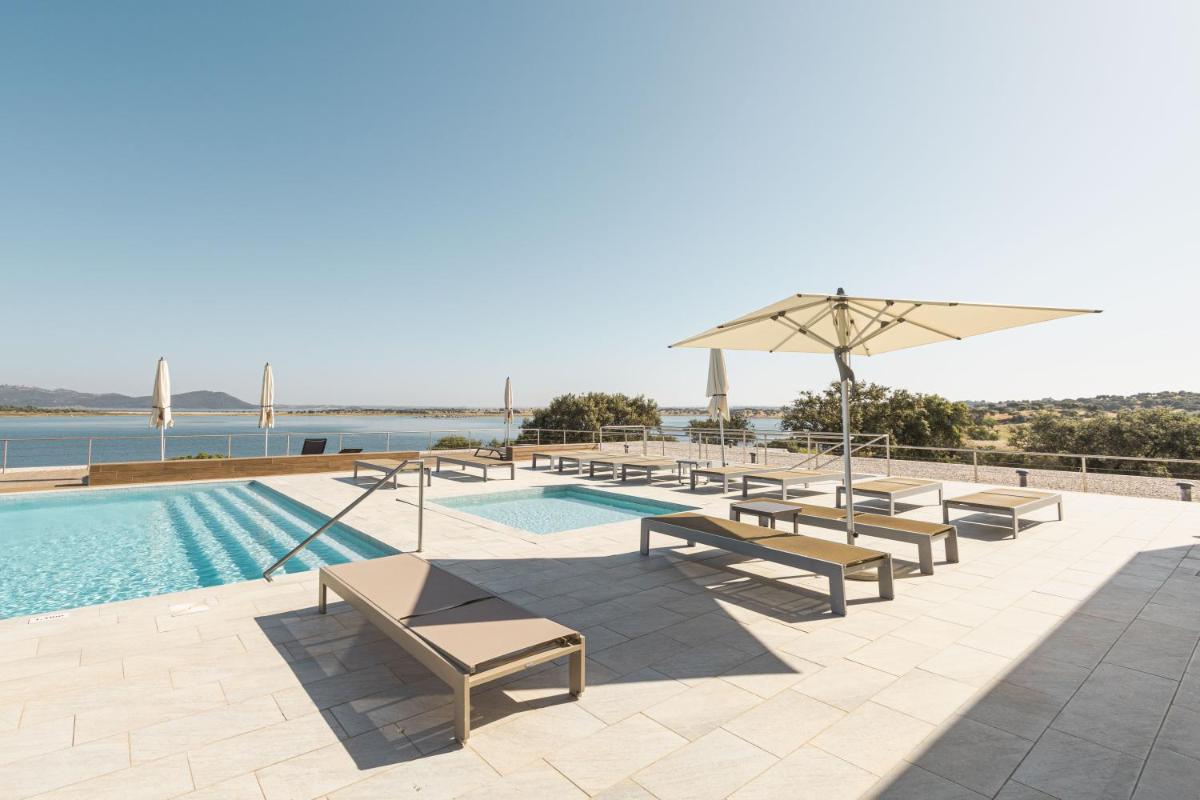 uma piscina com bancos e um guarda-sol junto à água em Herdade dos Delgados em Mourão