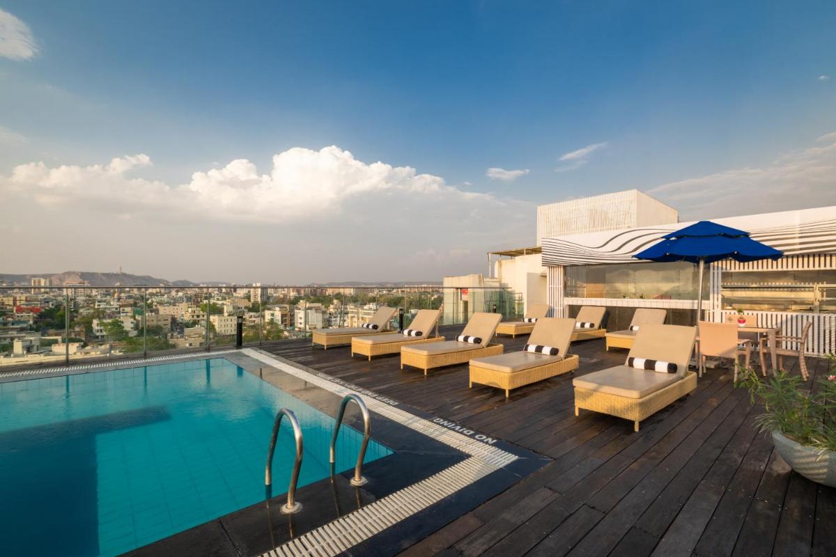 a swimming pool with chairs and an umbrella on a building at Sunday Hotel Jaipur in Jaipur