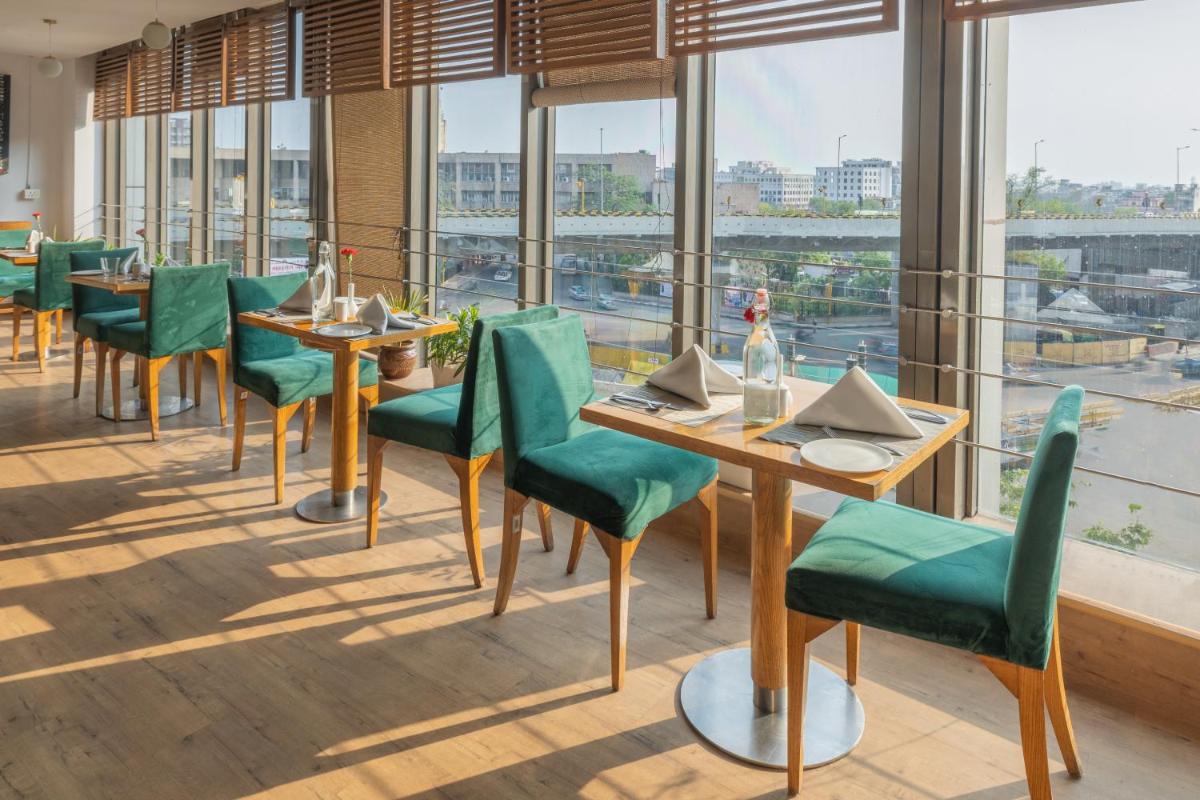 a restaurant with green chairs and tables and windows at Sunday Hotel Jaipur in Jaipur