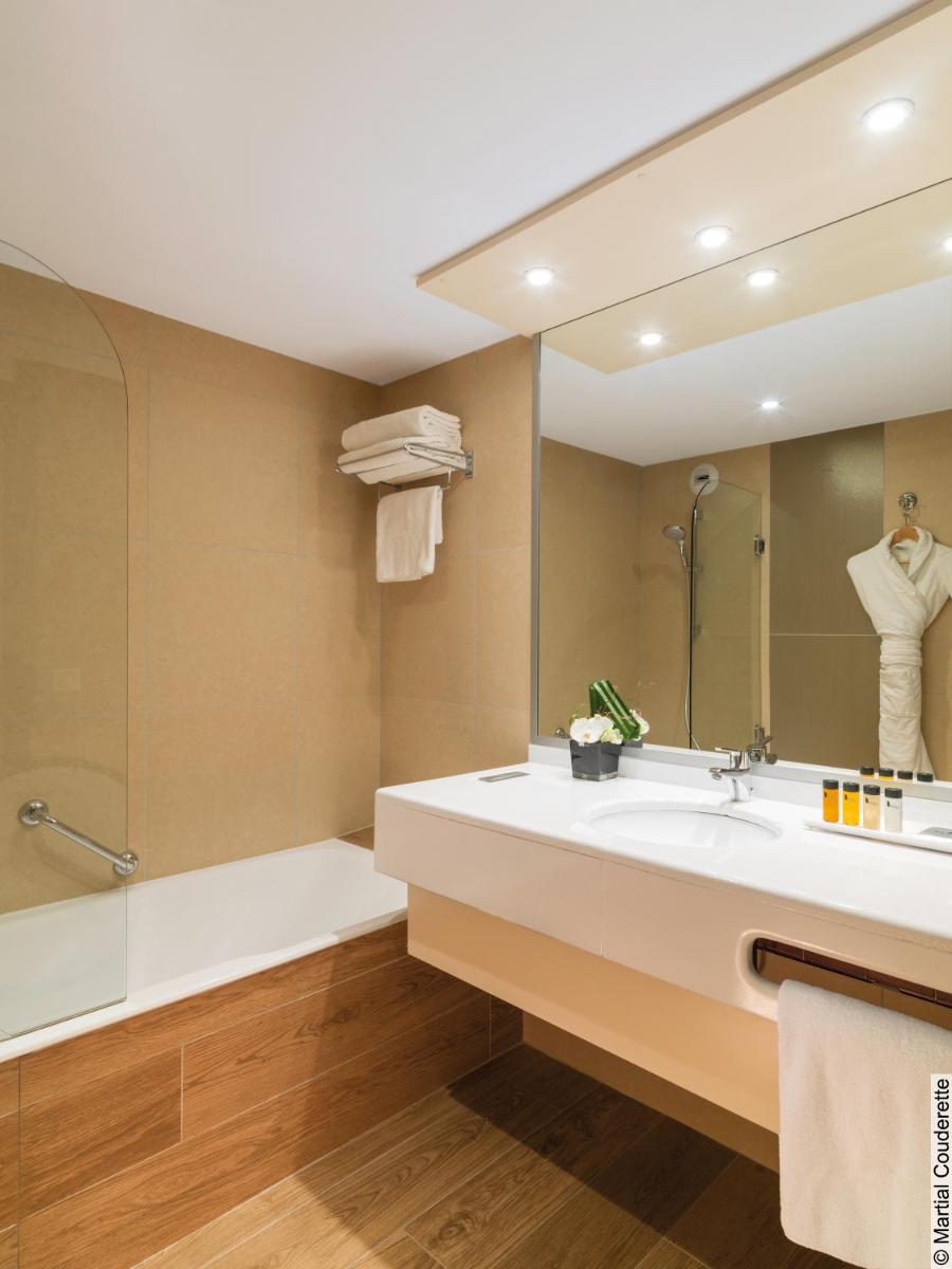 une salle de bains avec lavabo, baignoire et miroir dans l'établissement Hôtel Lyon Métropole & Spa, à Lyon