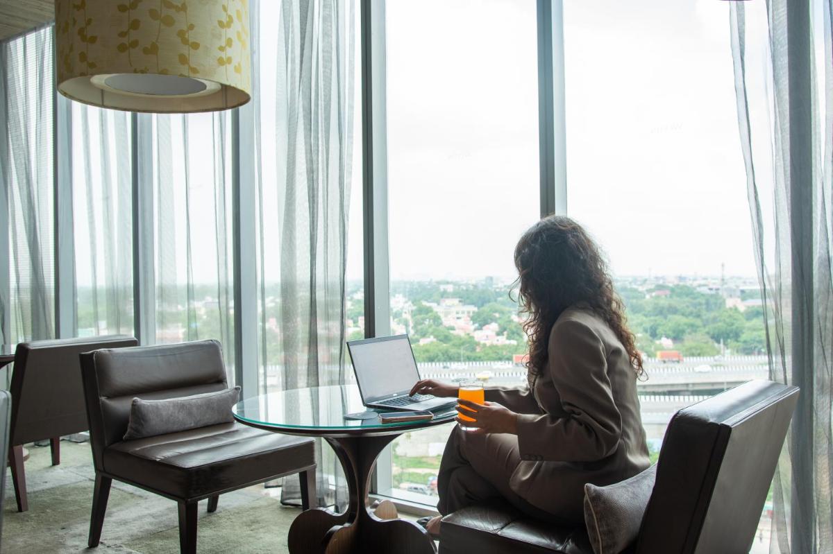 a woman sitting at a table with a laptop in front of a window at The Westin Gurgaon, New Delhi in Gurgaon