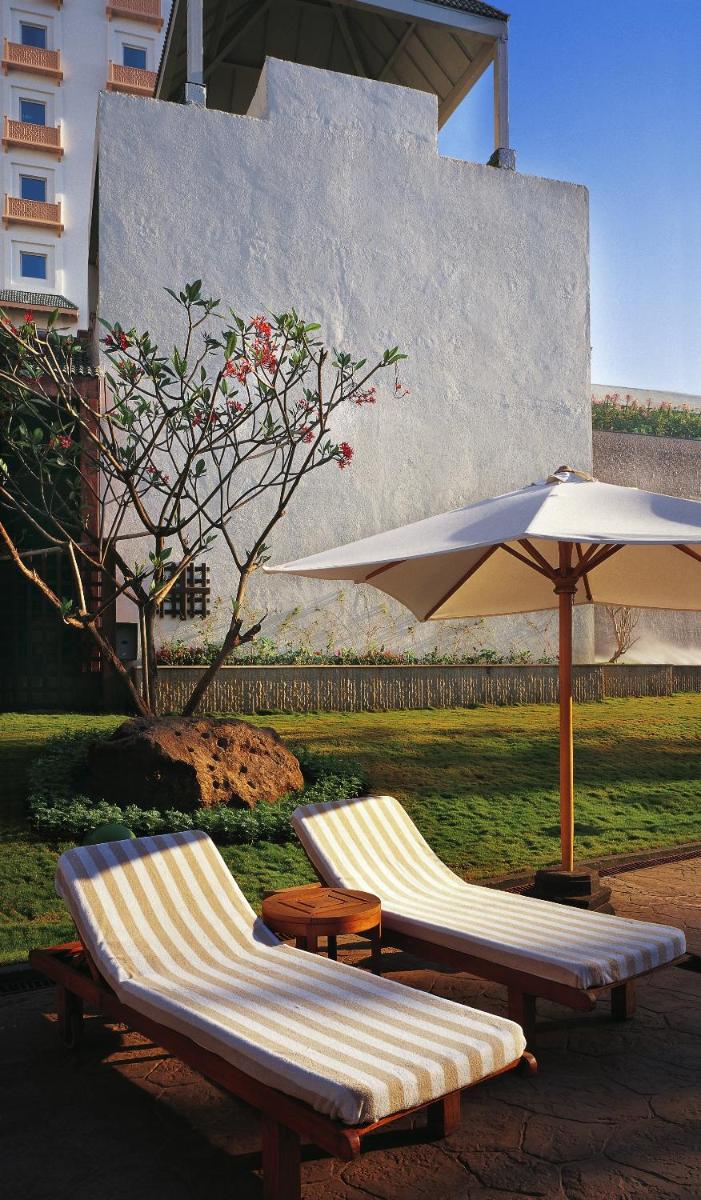 two lounge chairs and an umbrella next to a lawn at The Leela Mumbai in Mumbai two lounge chairs and an umbrella next to a lawn at The Leela Mumbai in Mumbai