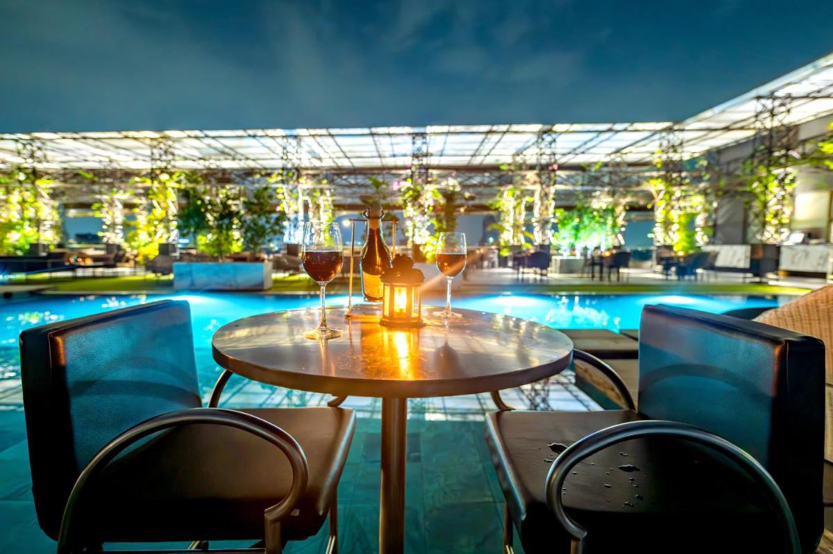 a table with glasses of wine next to a swimming pool at O Hotel Pune in Pune