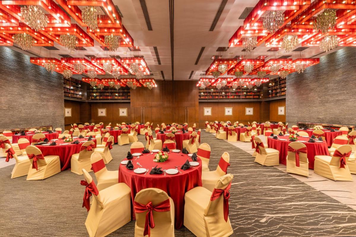 a banquet hall with red tables and chairs and chandeliers at O Hotel Pune in Pune