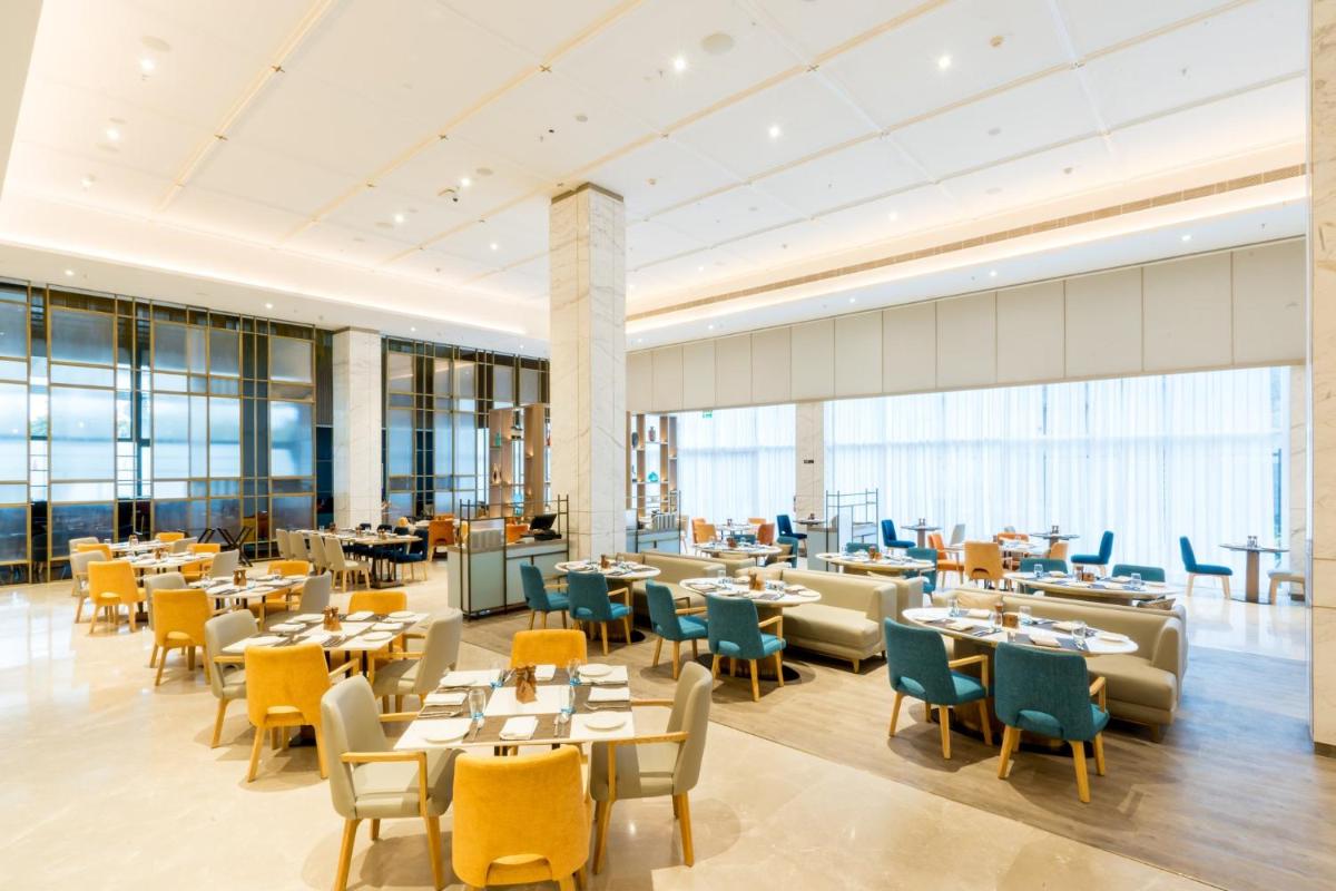 a restaurant with tables and chairs and windows at Holiday Inn Lucknow Airport by IHG in Lucknow