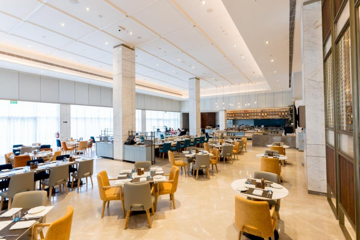 a restaurant with tables and chairs and a cafeteria at Holiday Inn Lucknow Airport by IHG in Lucknow