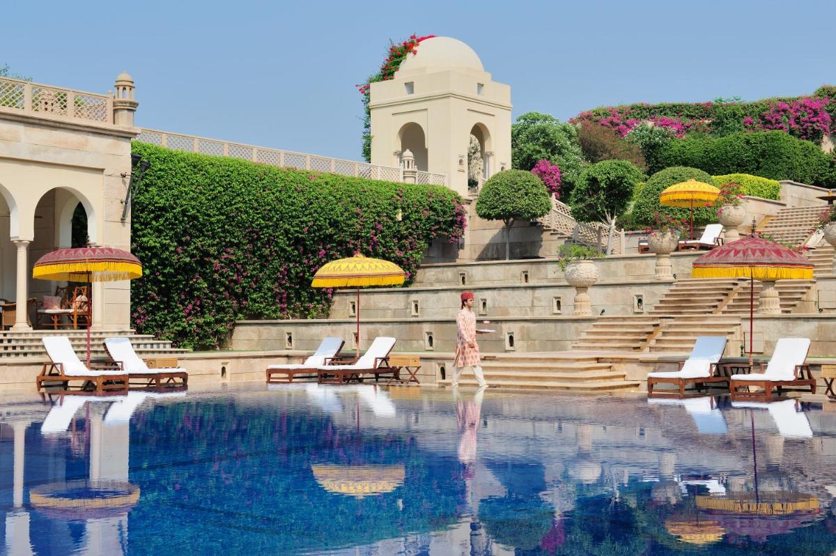 a woman standing next to a swimming pool with umbrellas at The Oberoi Amarvilas Agra in Agra