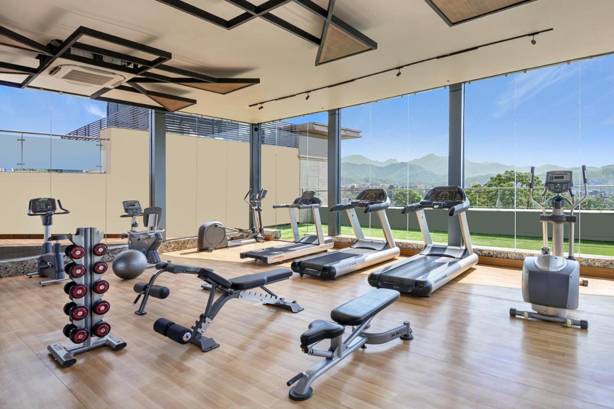 a gym with cardio equipment and large windows at Hyatt Centric Rajpur Road Dehradun in Dehradun