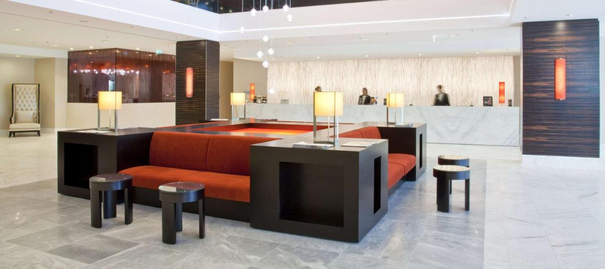 eine Lobby mit einem orangefarbenen Sofa und Hockern in der Unterkunft Hilton Mainz in Mainz eine Lobby mit einem orangefarbenen Sofa und Hockern in der Unterkunft Hilton Mainz in Mainz