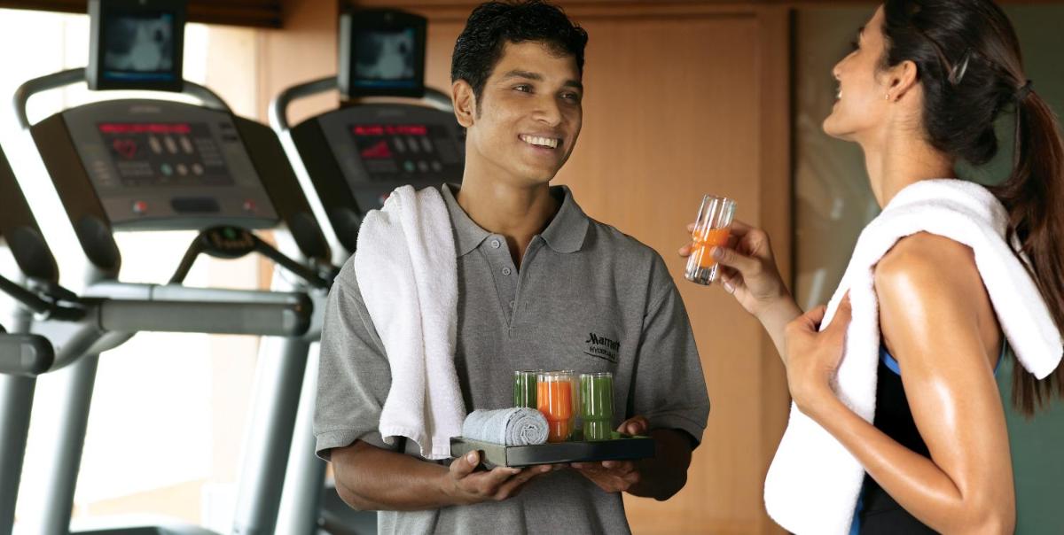 a man holding a tray of drinks in a gym with a woman at Hyderabad Marriott Hotel & Convention Centre in Hyderabad