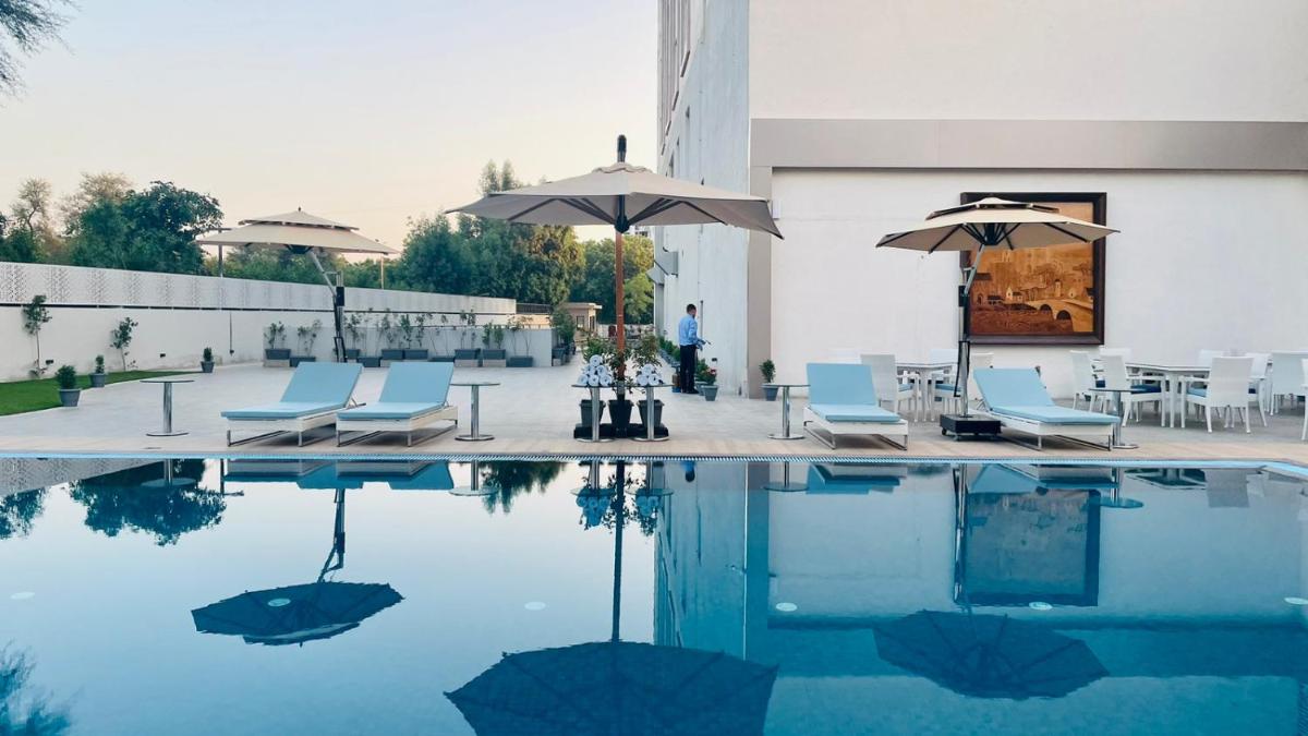 a pool with chairs and umbrellas next to a building at Vivanta Ahmedabad SG Highway in Ahmedabad